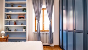 Una camera da letto con un letto, un comodino, una libreria, una finestra con tende e un armadio.