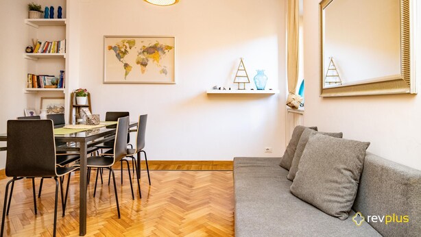 Zona pranzo con pavimento in parquet a spina di pesce, tavolo da pranzo con sedie, libreria, mappa del mondo e specchio con cornice decorativa.