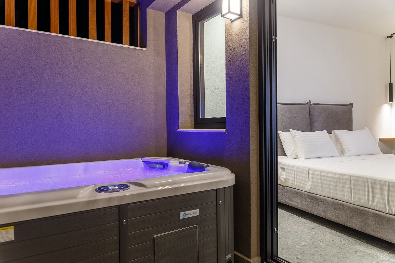 Ein modernes Badezimmer mit Fußbodenheizung, einem Waschtisch mit Spiegel und einem Bett mit Kopfteil im angrenzenden Raum.