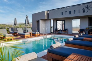Uma área de piscina no terraço com espreguiçadeiras e guarda-sóis, um deck de madeira e um edifício com a placa "UTOPIA".
