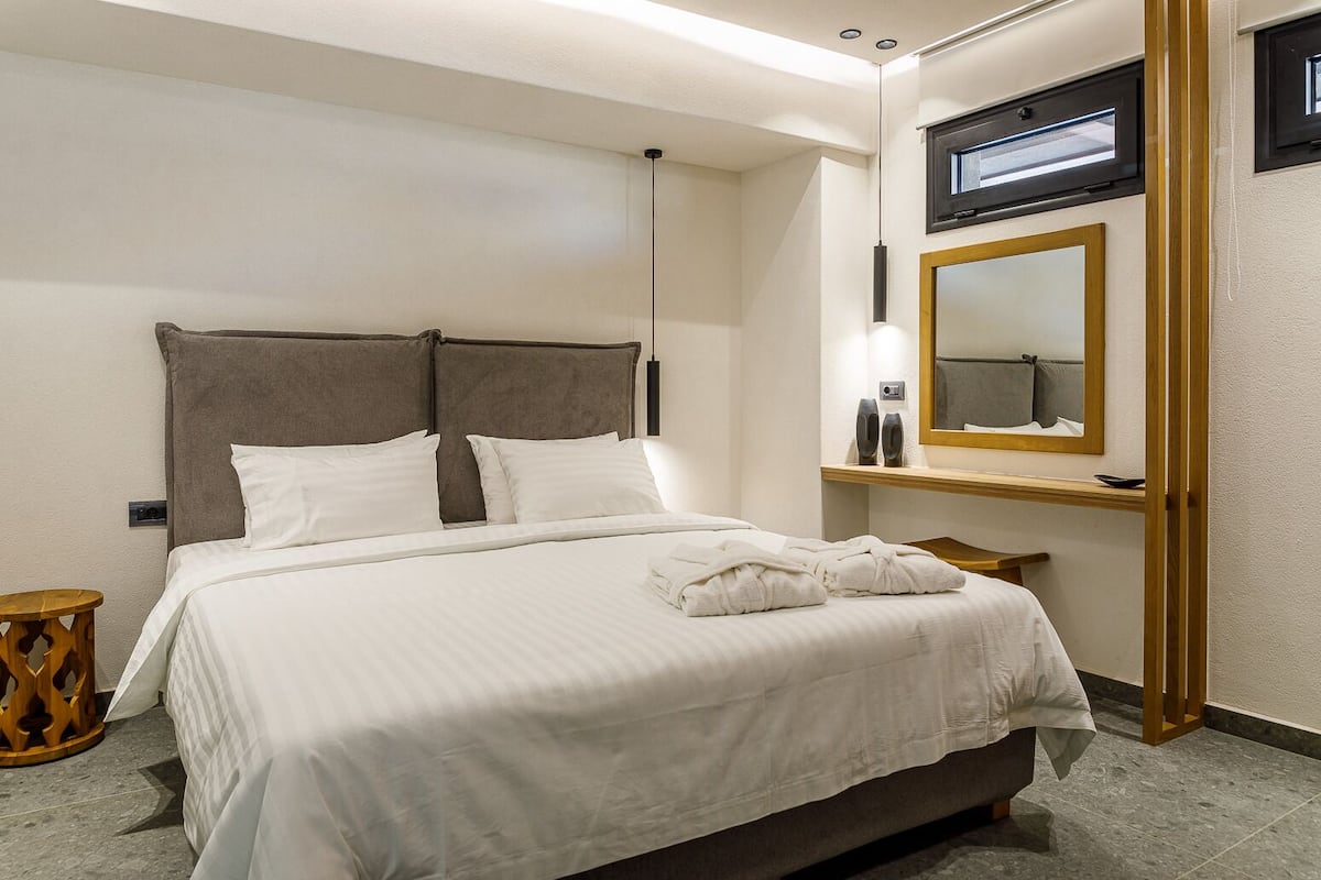 A hotel room with a large bed, a bedside table, a mirror, and a small wooden stool.