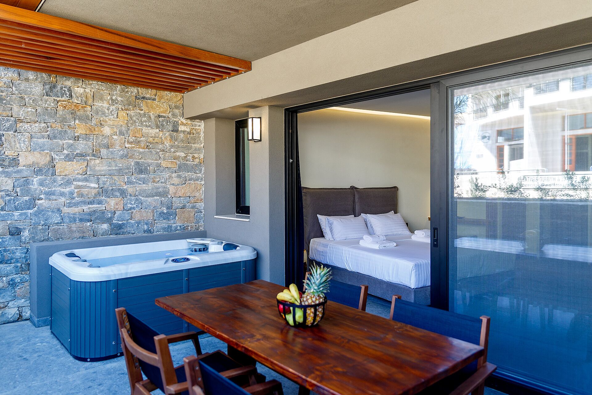 A room with a stone wall, a wooden ceiling, a hot tub, a bed, and a table with fruit.