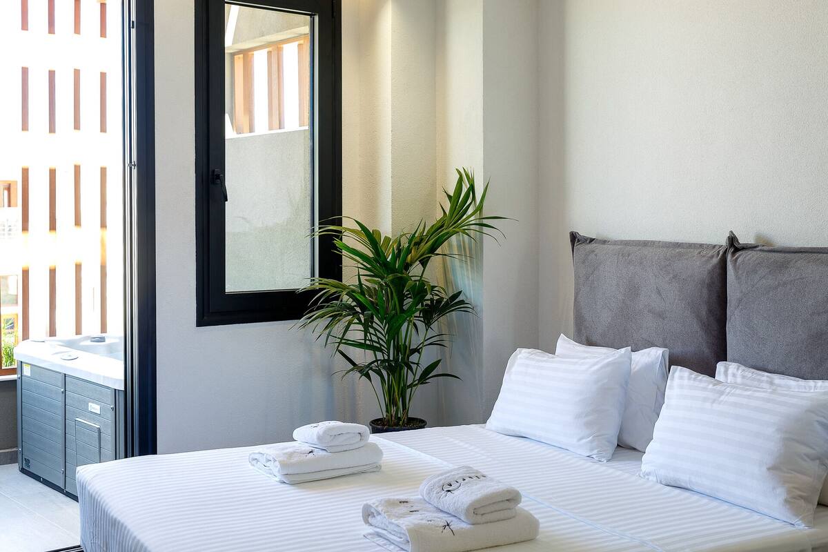 A hotel room with a bed, pillows, a plant, and a window.