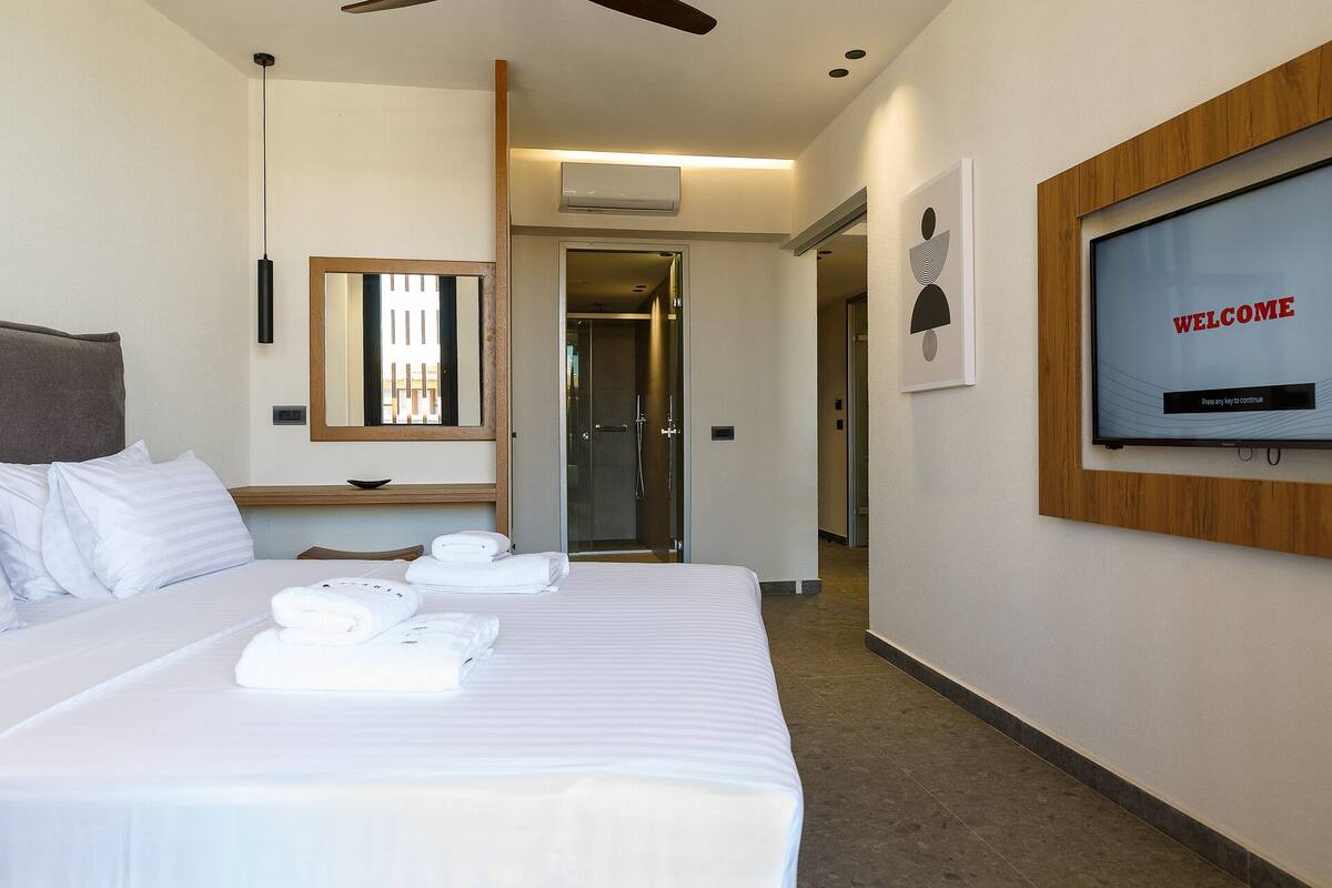 A hotel room with a bed, a TV displaying 'WELCOME', a mirror, and a door leading to a bathroom.