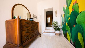 Un couloir avec une commode en bois, un miroir et une fresque représentant un cactus sur le mur.