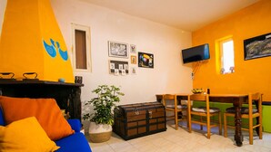 Un salon avec un canapé bleu, des coussins orange, une table en bois avec des chaises, un téléviseur et divers éléments de décoration murale.