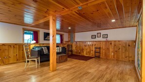 Une pièce spacieuse avec un plancher en bois, un canapé, un fauteuil et un lambris en bois.