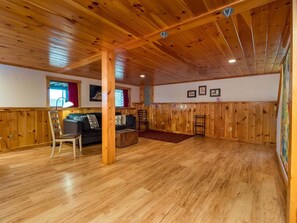 A spacious room with wooden flooring, a sofa, a chair, and a wooden wall paneling.