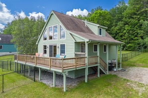 A light green house with a porch, a covered deck, and a staircase leading to the main entrance.