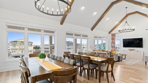 A spacious dining area with a long wooden table, multiple chairs, and a chandelier. - Big Orange Beach House by Brunswick Vacation Rentals: Heated Pool & Great Views (Ocean Isle Beach)