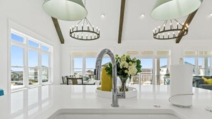 A modern kitchen with a central island, large windows, and a view of the outdoors. - Big Orange Beach House by Brunswick Vacation Rentals: Heated Pool & Great Views (Ocean Isle Beach)