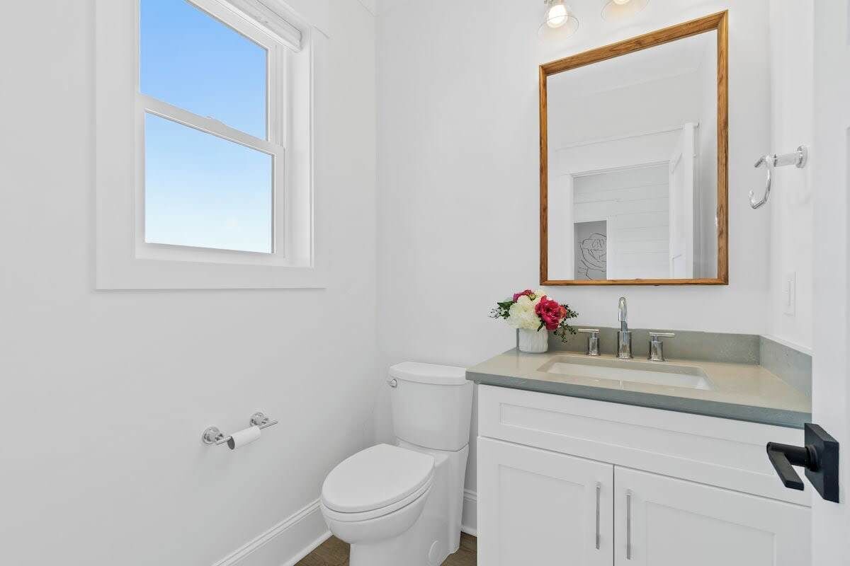 A bathroom with a toilet, sink, mirror, and window.