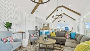 A spacious living room with a high ceiling, a dining area, and a kitchen in the background. - Big Orange Beach House by Brunswick Vacation Rentals: Heated Pool & Great Views (Ocean Isle Beach)