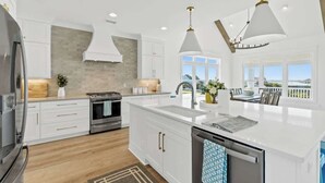 A modern kitchen with white cabinetry, stainless steel appliances, and pendant lighting. - Big Orange Beach House by Brunswick Vacation Rentals: Heated Pool & Great Views (Ocean Isle Beach)