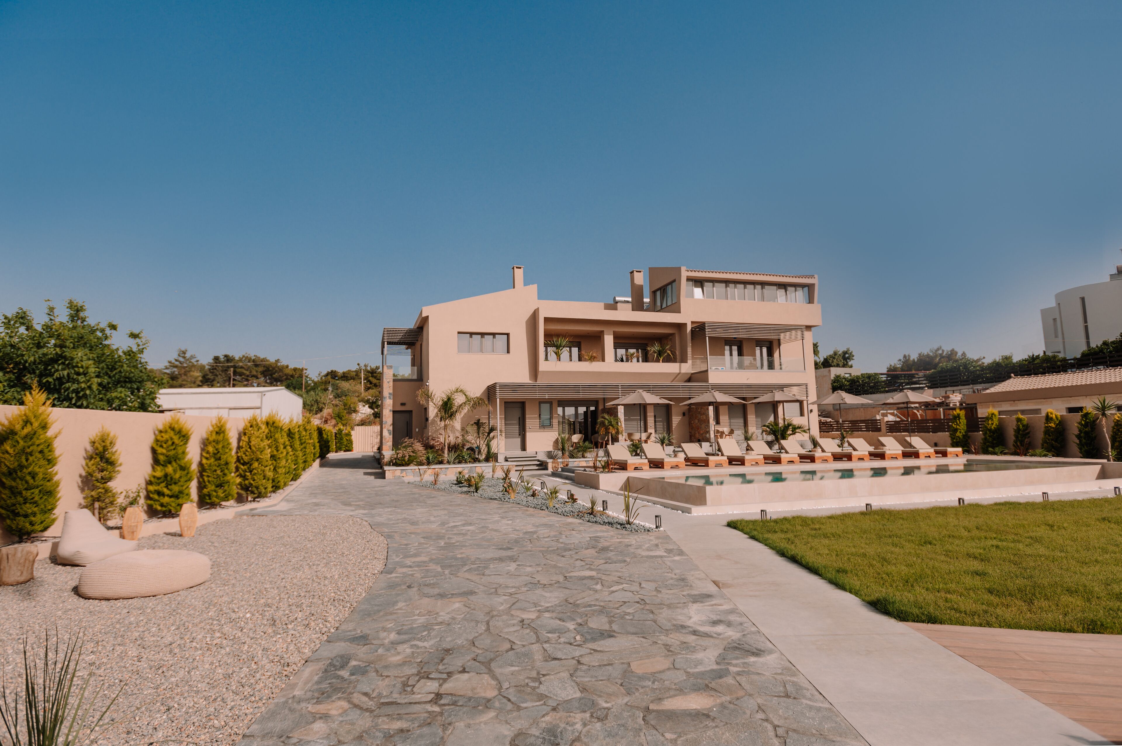 Una casa moderna de dos pisos con piscina, mobiliario exterior y un jardín cuidado.