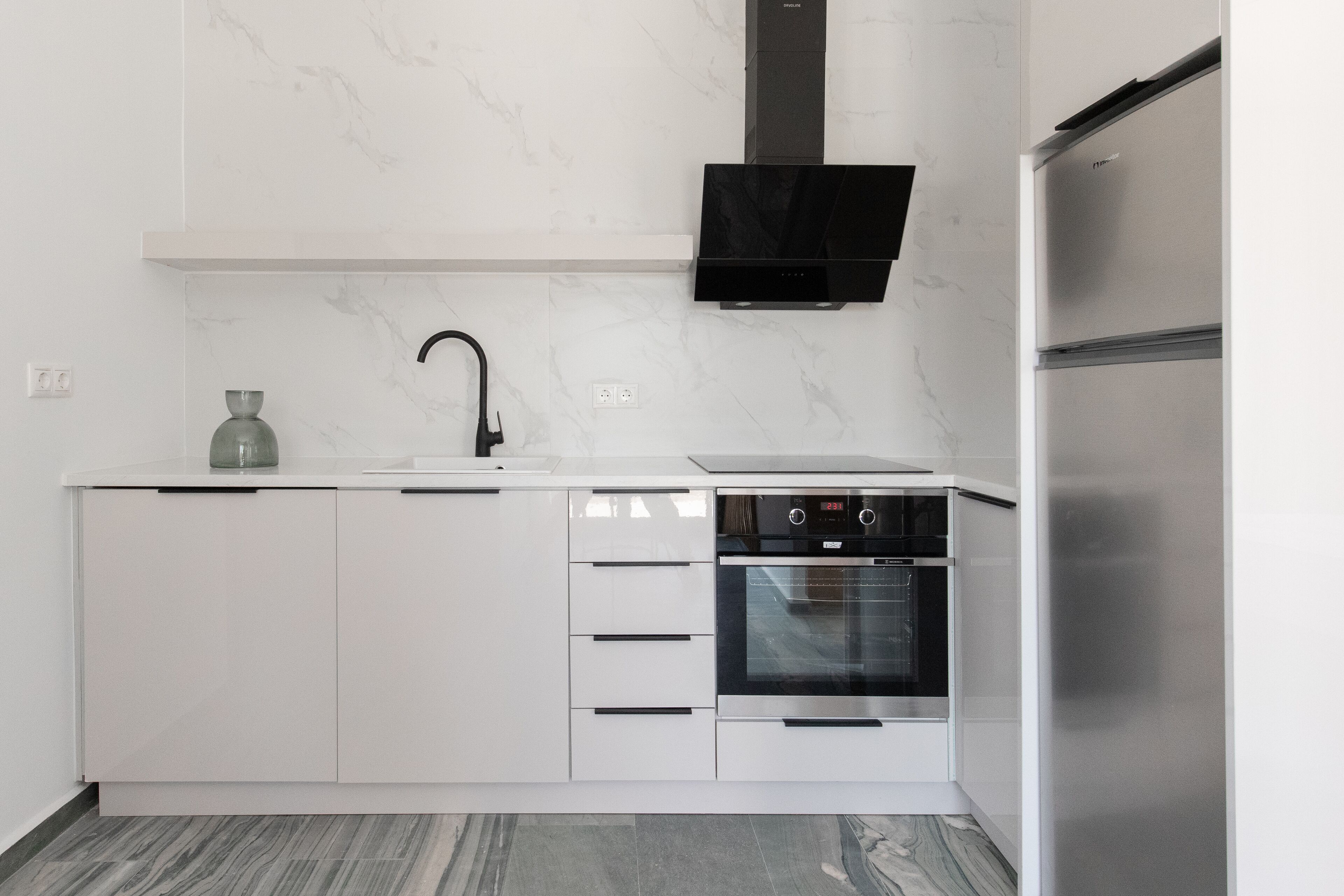 A modern kitchen with white cabinetry, a stainless steel oven, and a black range hood.