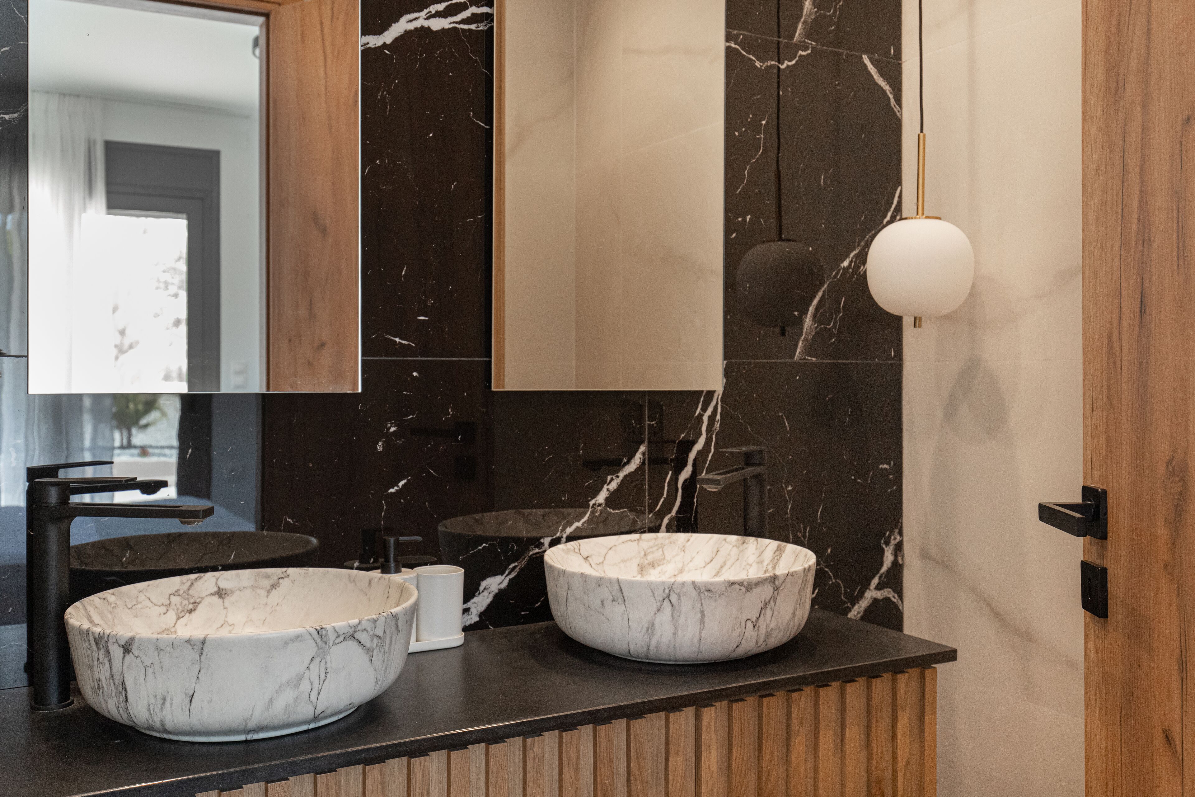 A modern bathroom with two marble sinks, a wooden vanity, and a large mirror.