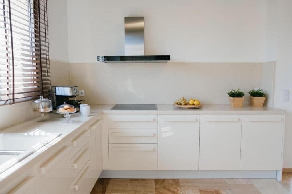 Una cucina moderna con mobili bianchi, una cappa in acciaio inossidabile, un lavello e una finestra con persiane.