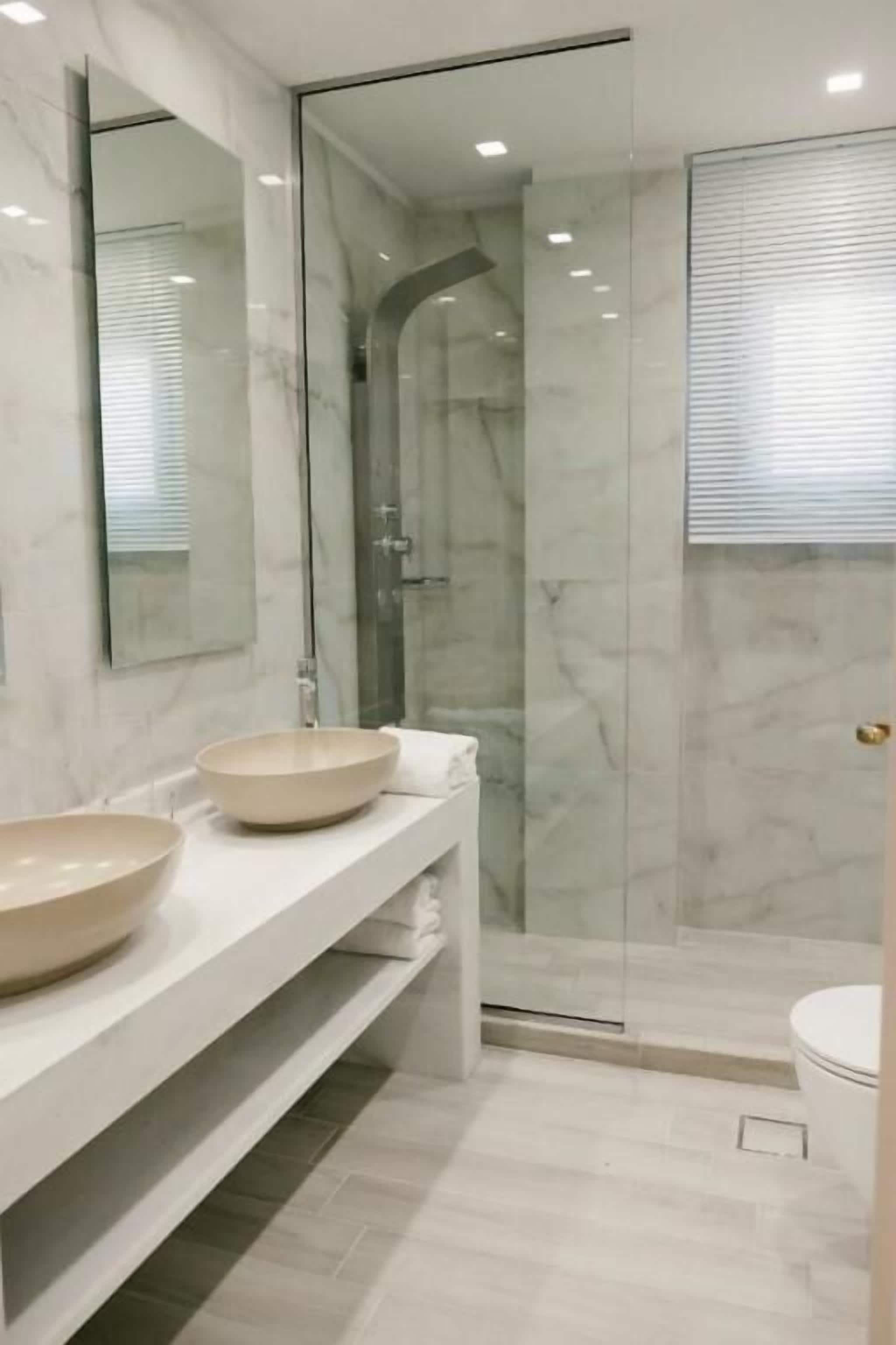 A modern bathroom with two large sinks, a glass-enclosed shower, and a white toilet.
