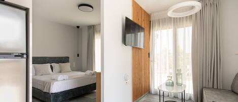A modern hotel room with a bed, a TV, a sofa, and a small table.