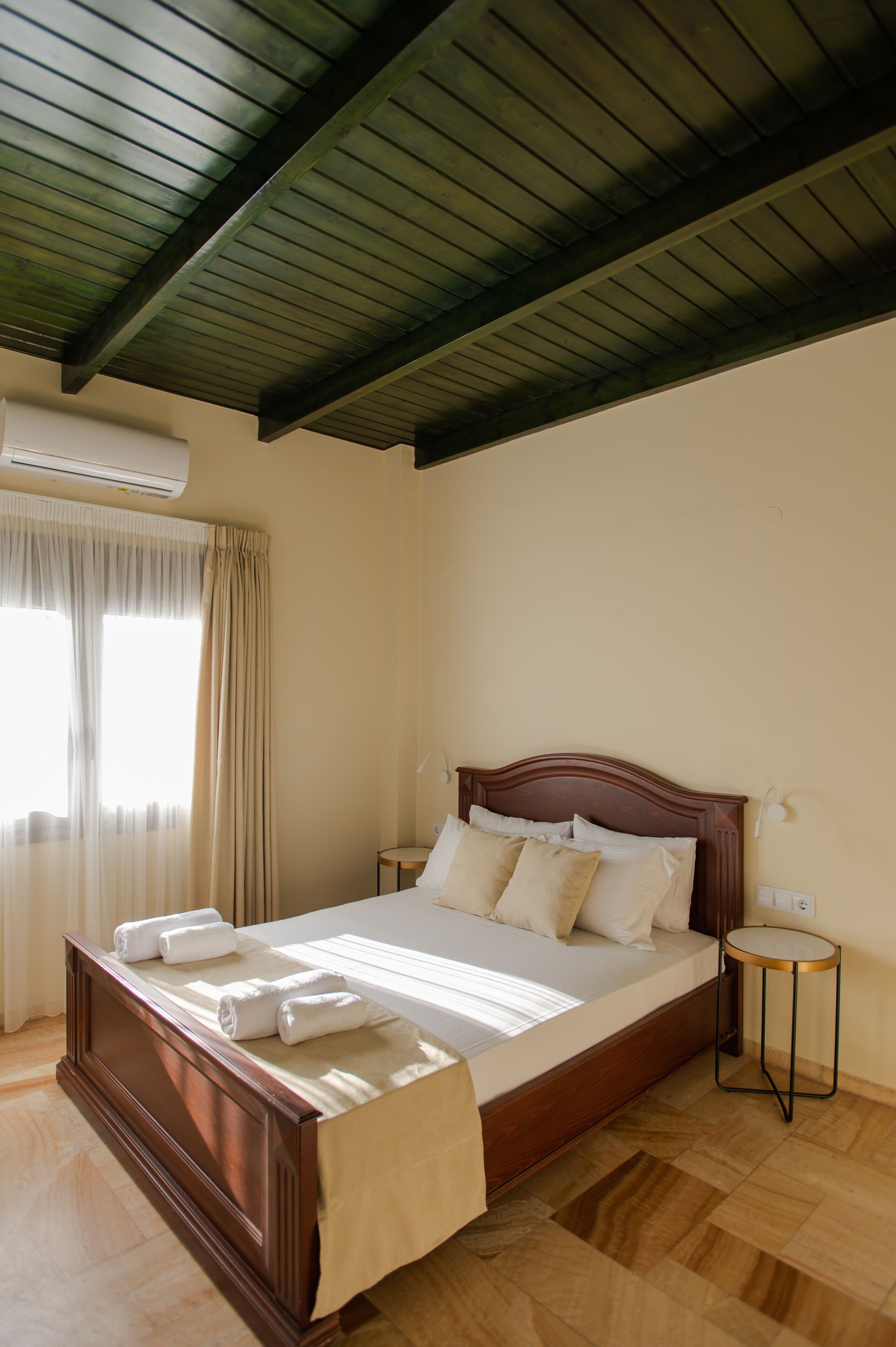 A bedroom with a wooden bed, beige curtains, and a small bedside table.
