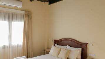 A bedroom with a wooden bed, beige curtains, and a small bedside table.
