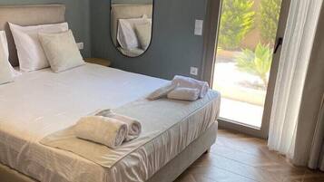 A bedroom with a large bed, a mirror, and a sliding glass door leading to an outdoor area.