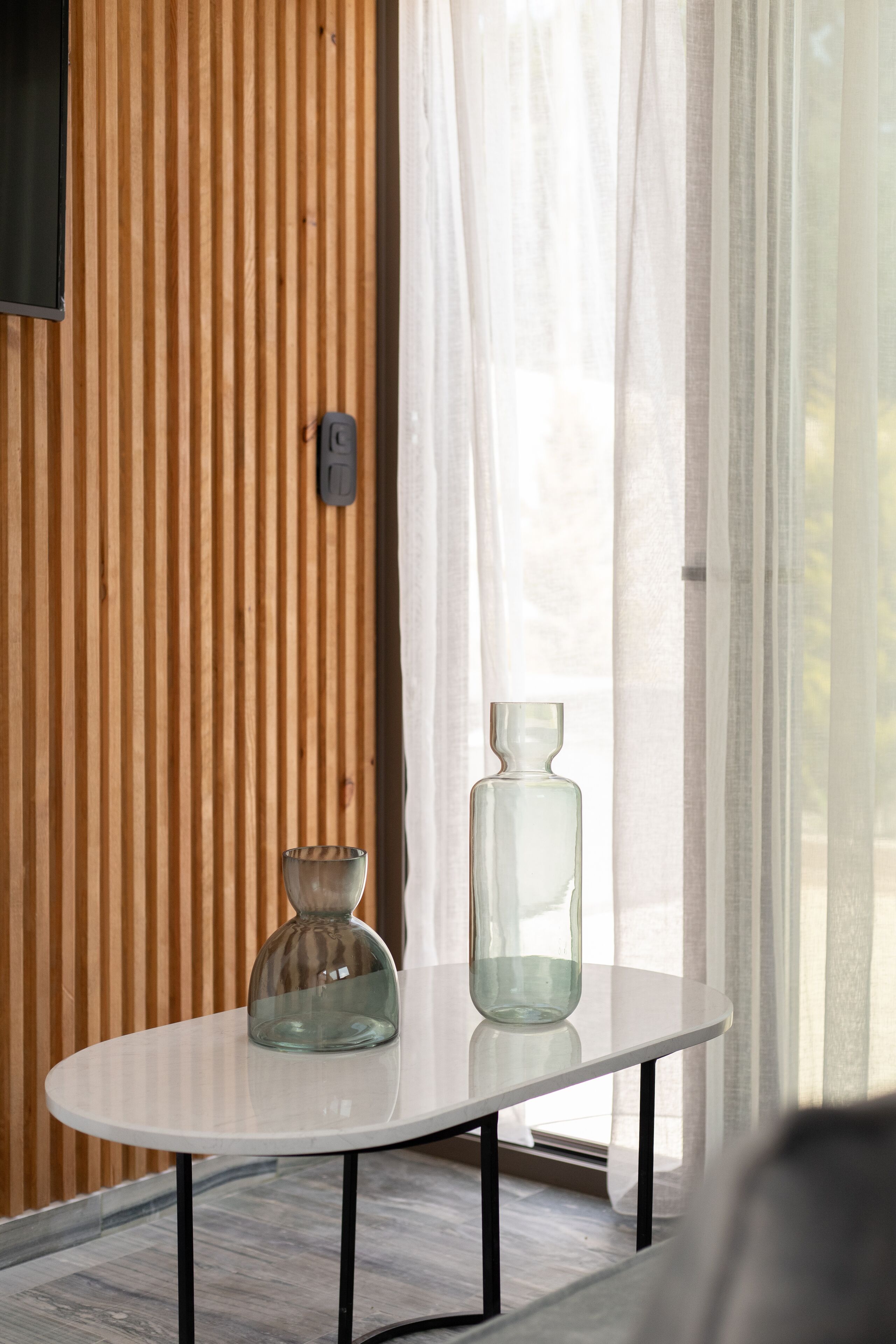 A modern room with a white table, two glass vases, and a wooden slat wall.