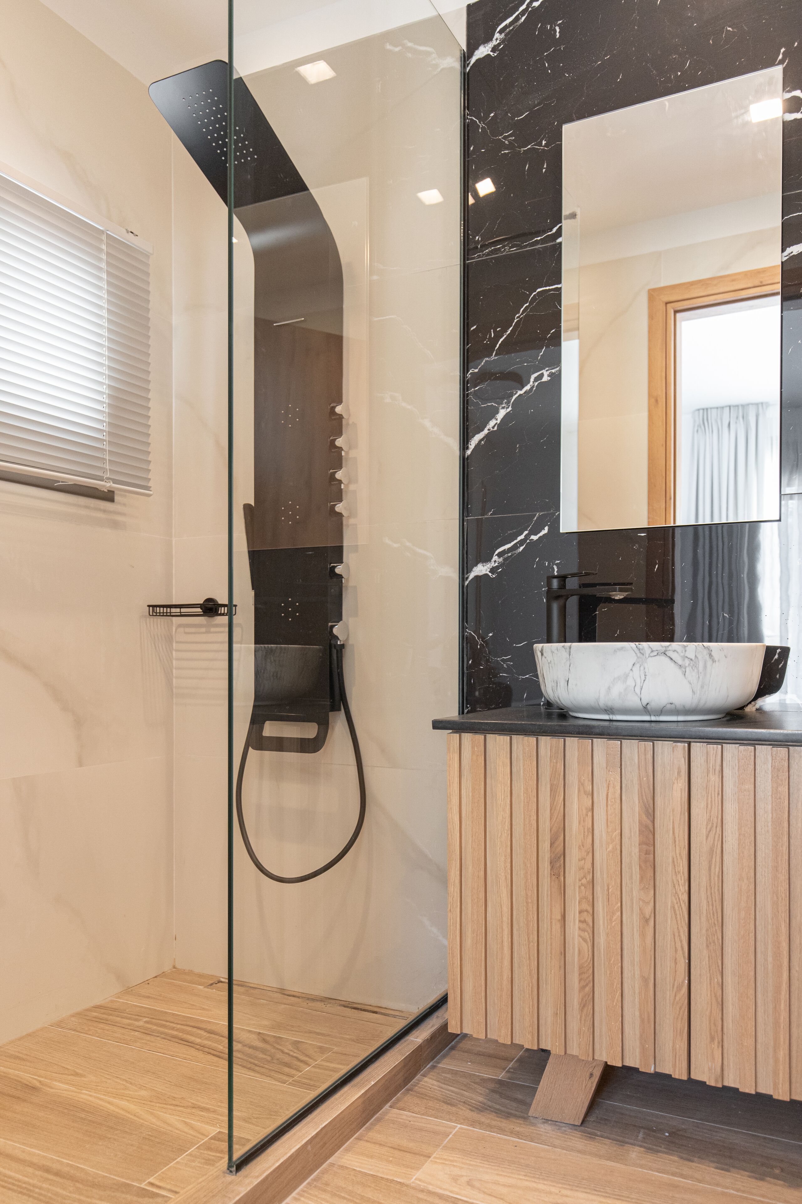 A modern bathroom with a glass-enclosed shower, a wooden vanity, and a marble sink.