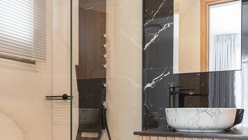 A modern bathroom with a glass-enclosed shower, a wooden vanity, and a marble sink.