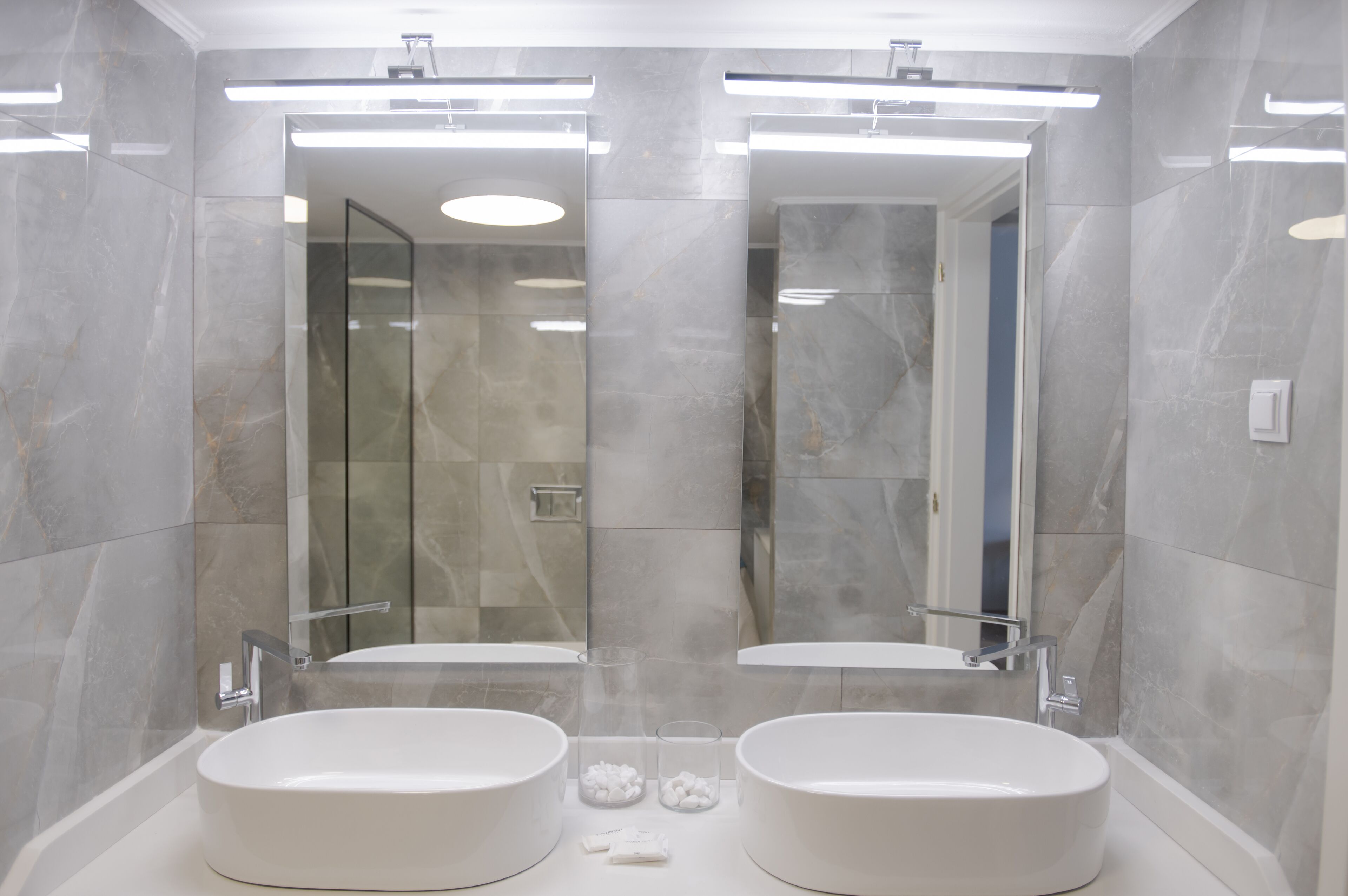 Een moderne badkamer met twee grote ovale wasbakken, een glazen douchecabine en een spiegel boven elke wasbak.