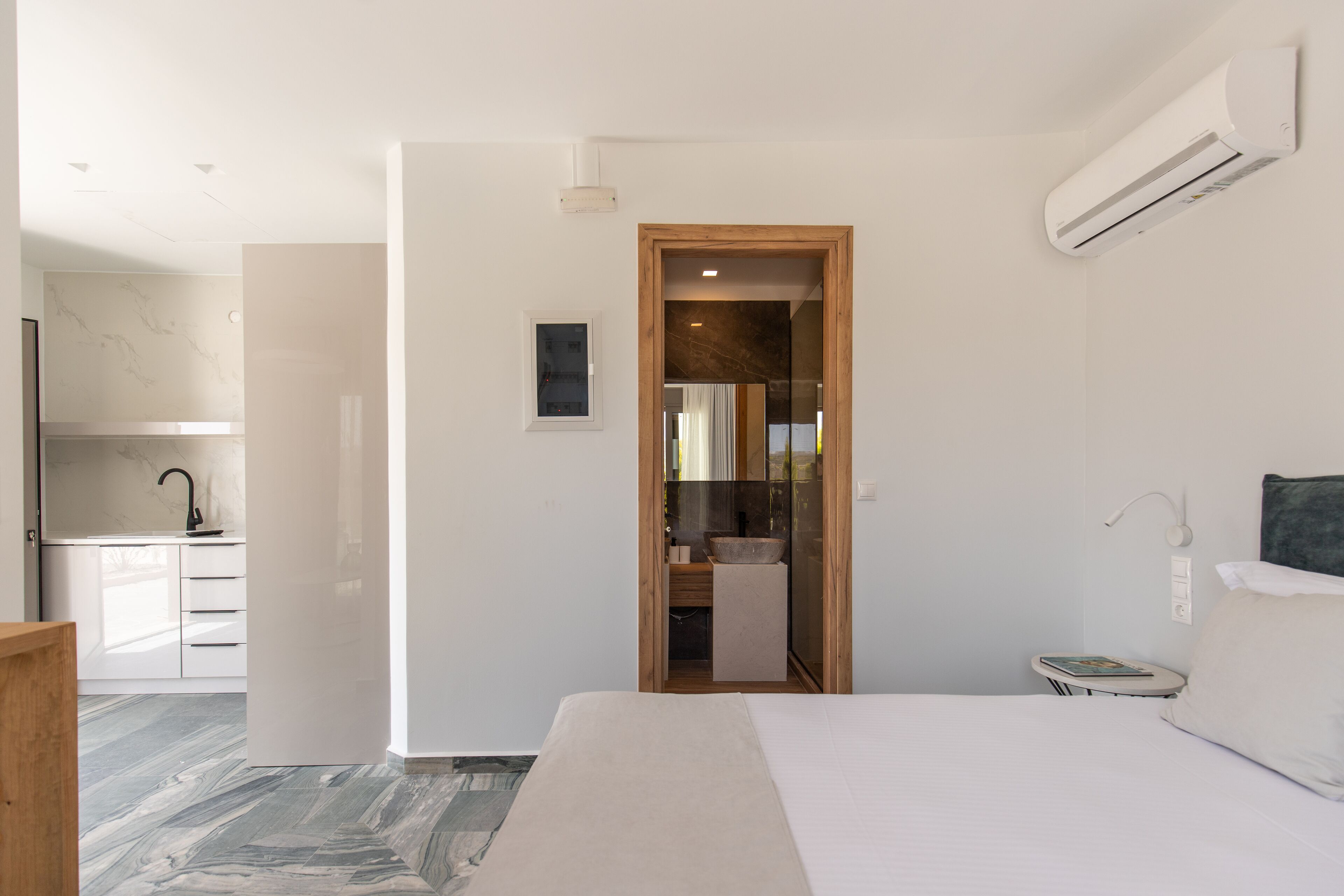 Een moderne hotelkamer met een groot bed, een houten deur naar een badkamer, een klein nachtkastje en een wandairconditioner.