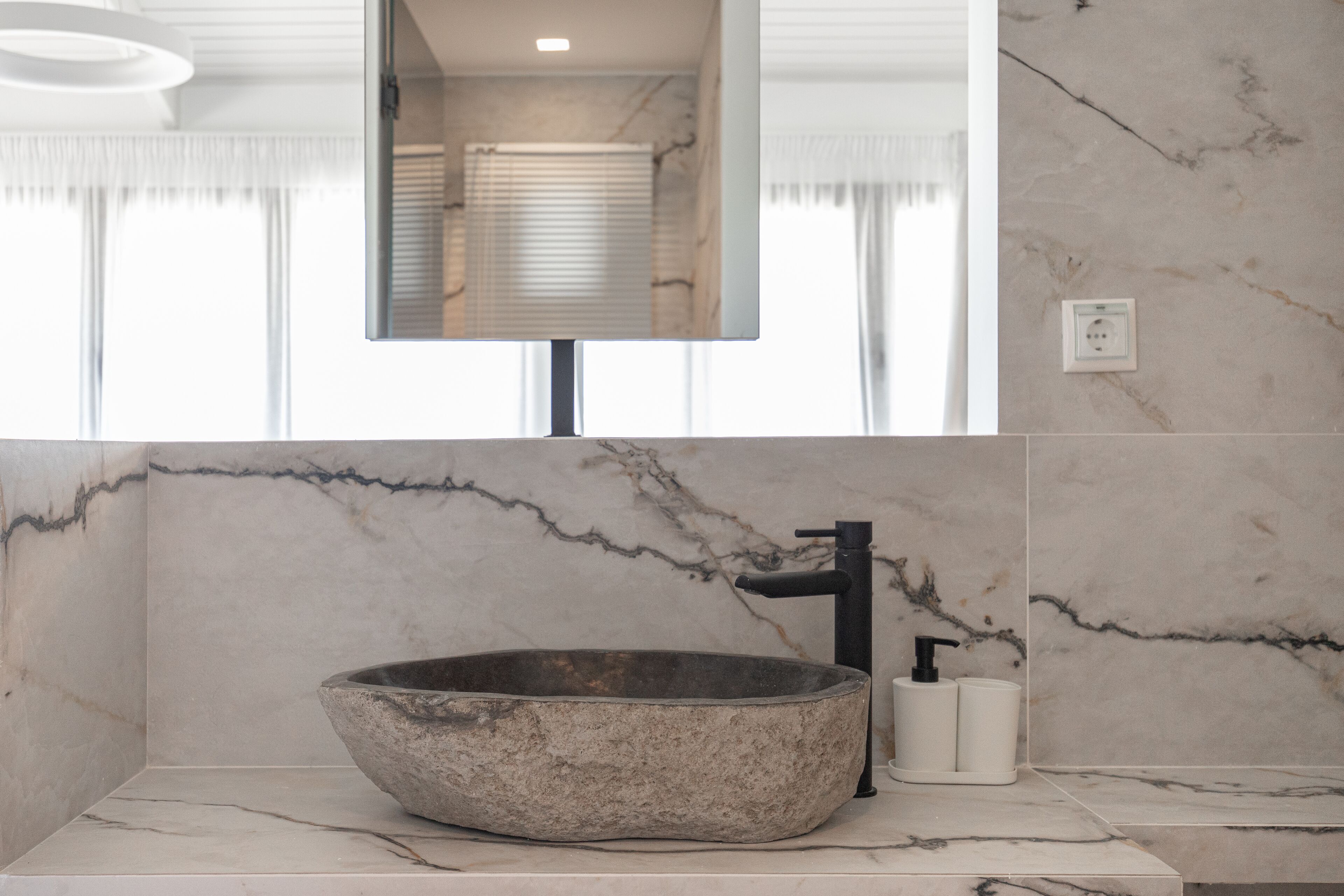 Un baño con un lavamanos grande y redondo de piedra, un grifo negro y un espejo encima.