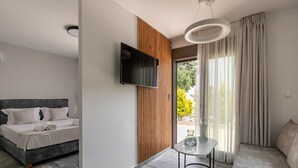 A modern hotel room with a bed, a TV, a seating area, and a view of the outdoors. - Marble Luxury Suites (Heraklion)