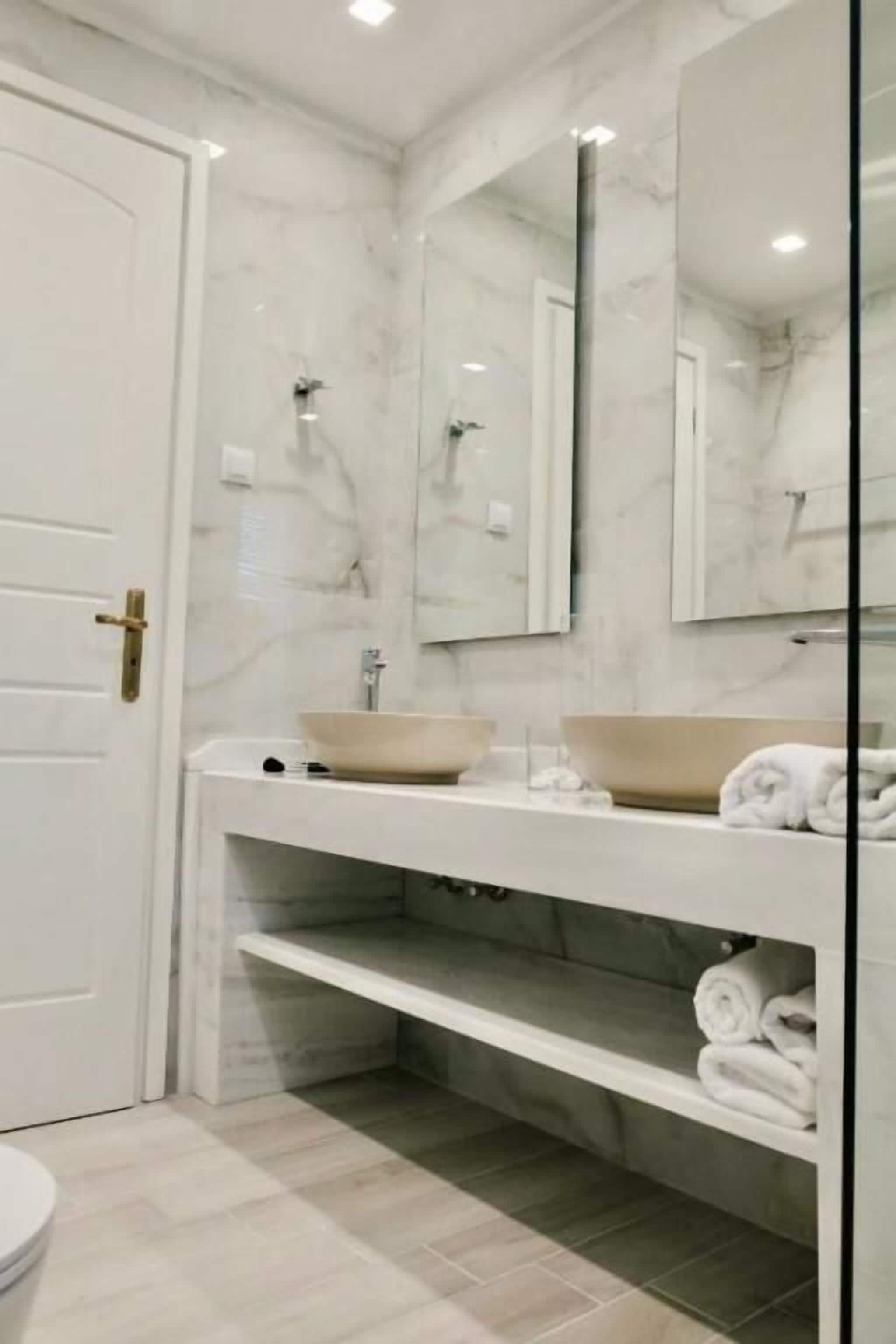 A modern bathroom with a marble backsplash, a large mirror, a sink with a bowl basin, and a toilet.