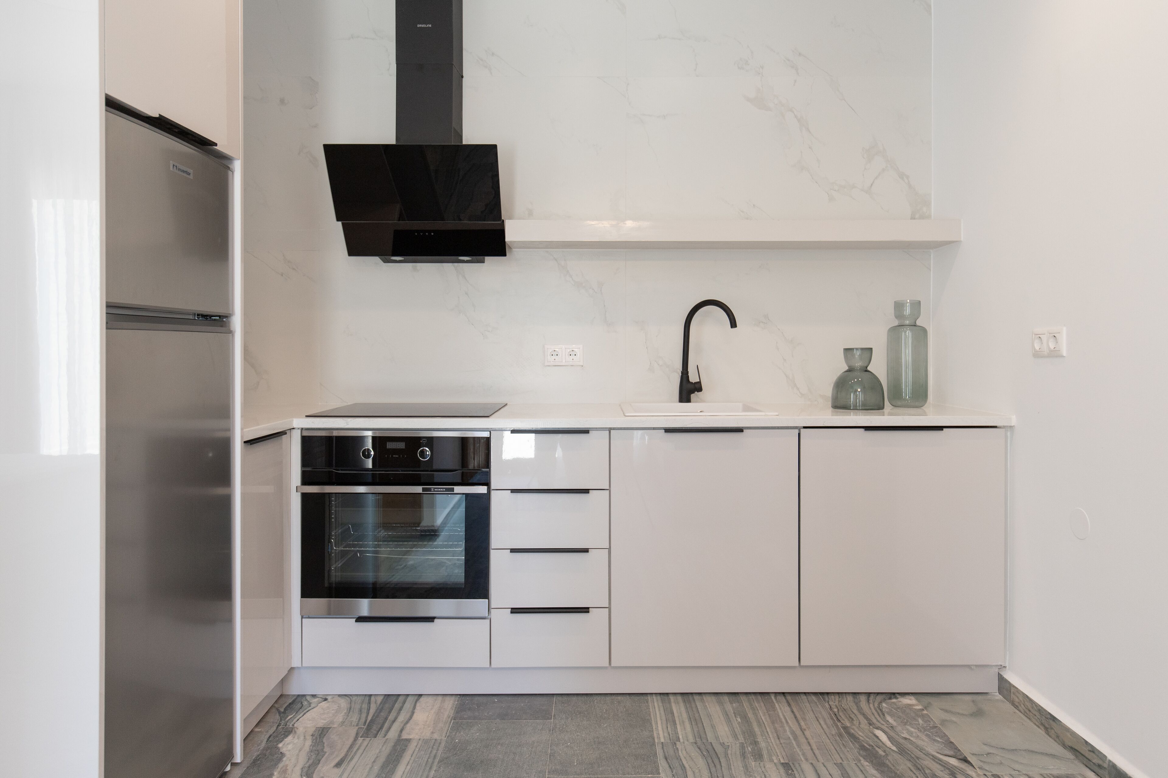 A modern kitchen with white cabinetry, a built-in oven, a microwave, and a black range hood.