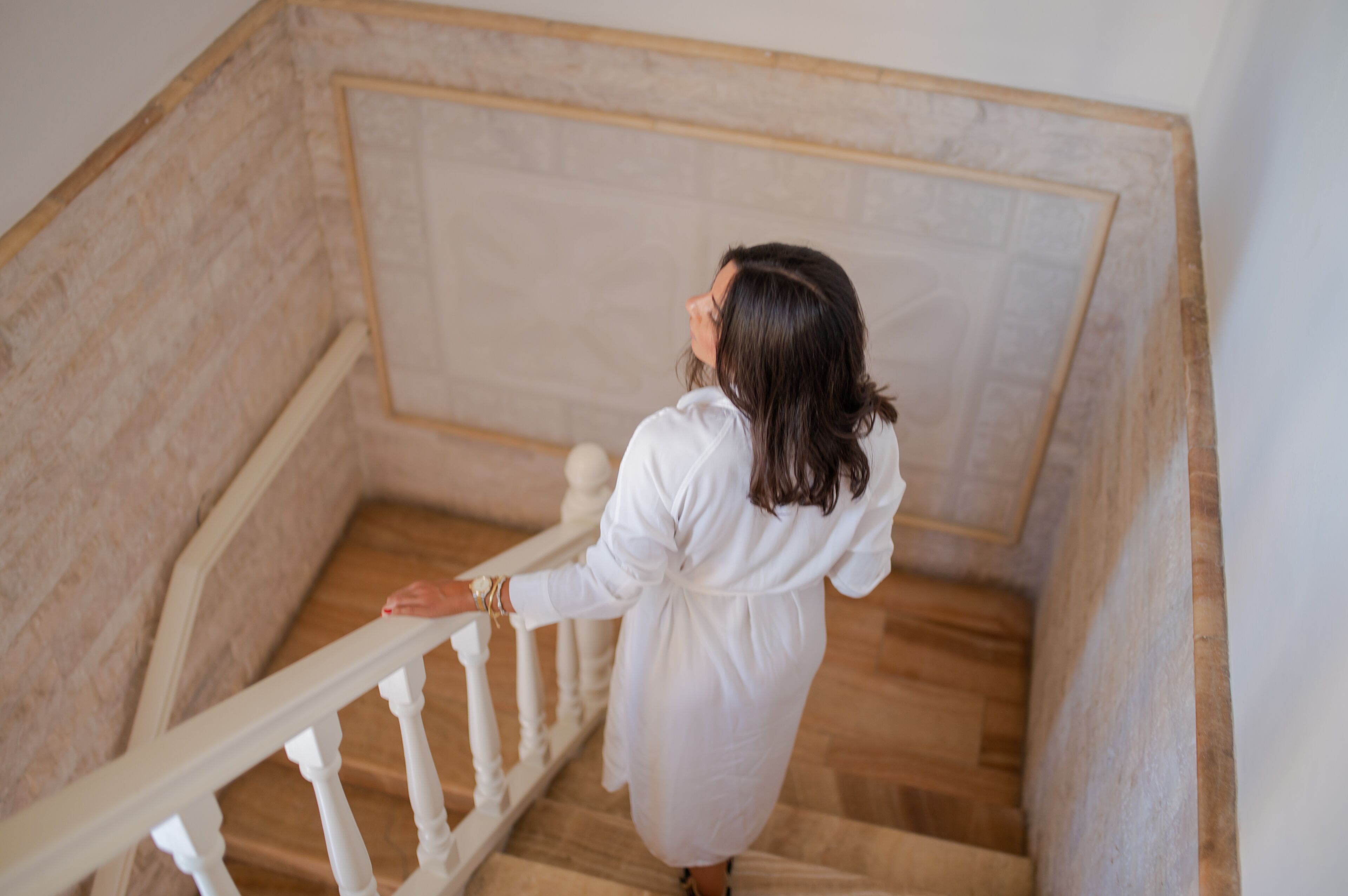 A woman descending a wooden staircase with white balusters.