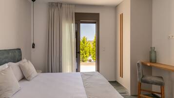 Ein Schlafzimmer mit Bett, Stuhl, Schreibtisch und Blick auf Grünanlage durch eine Tür.