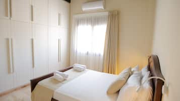 A neatly made bed with white linens and pillows, a bedside table, and a wardrobe with a mirror.