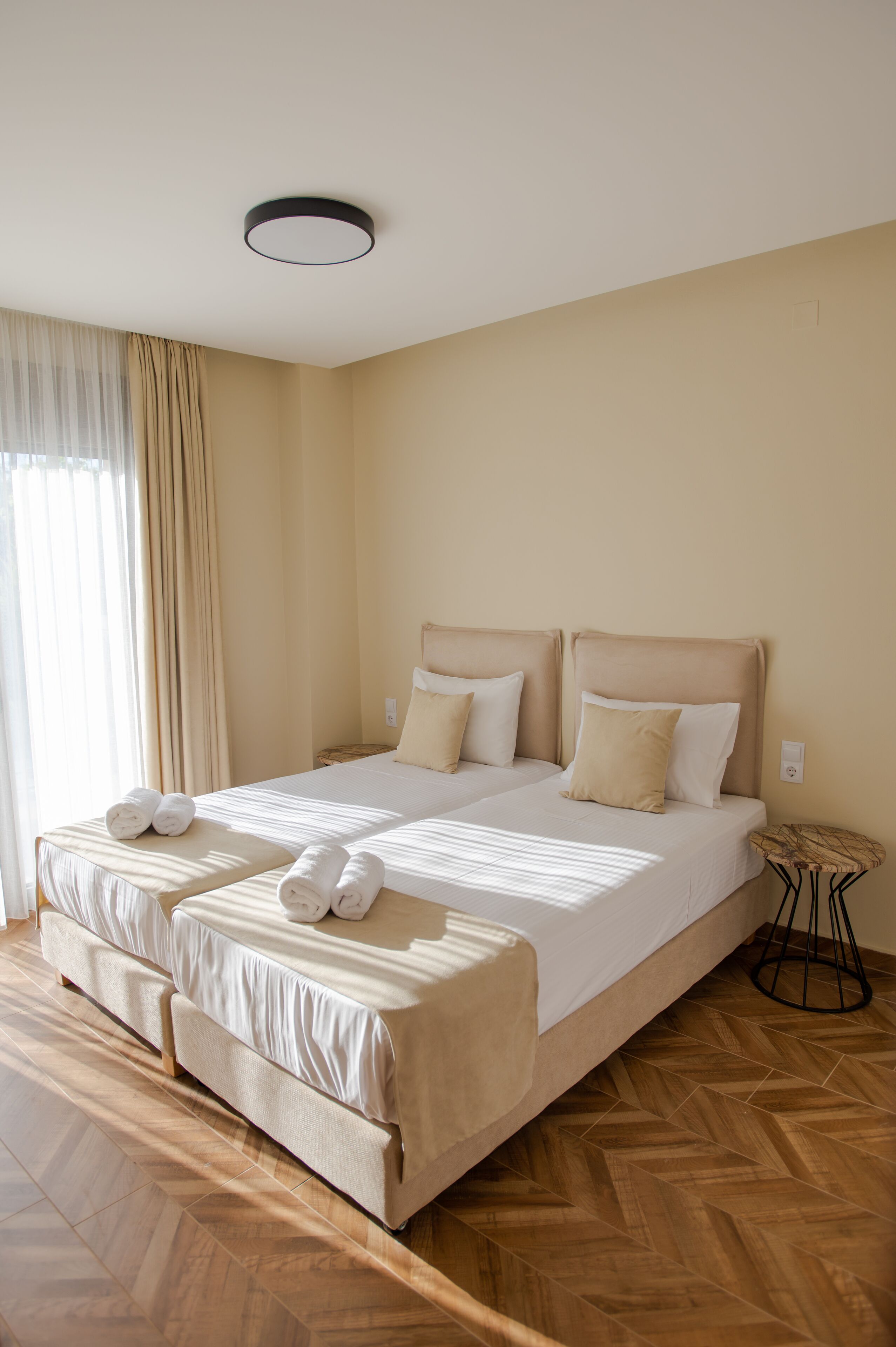 Uma cama de casal com cabeceira, duas almofadas e toalhas enroladas no rodapé.