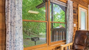 Ein Zimmer in einer Holzhütte mit einem großen Fenster, einem braunen Ledersessel und einem Briefkasten davor.