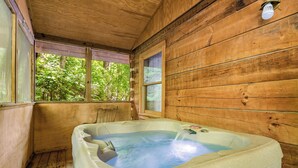 Eine Holzhütte mit Whirlpool, Holzfassade und einem Fenster mit Blick auf Grünflächen.