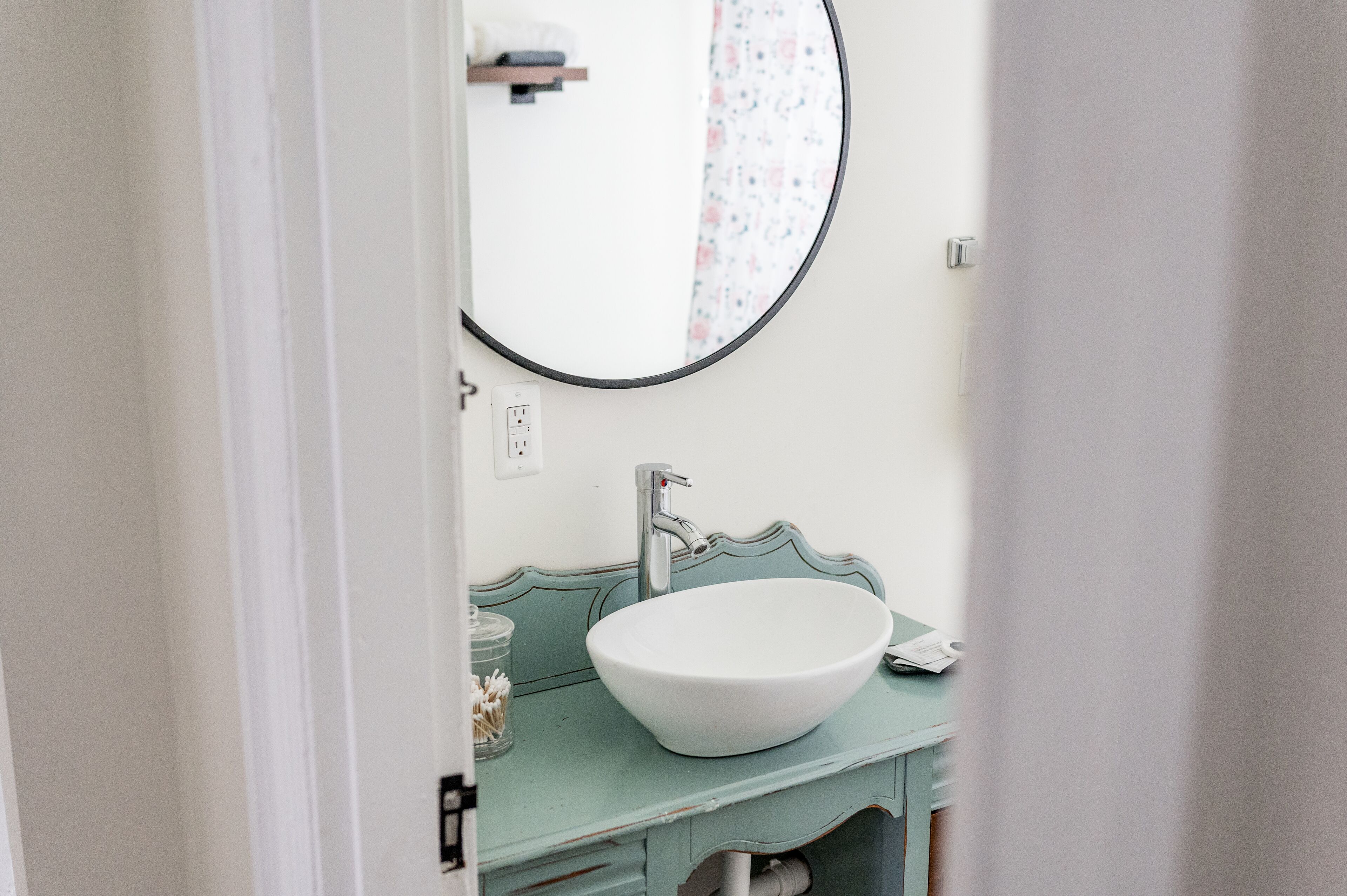 A bathroom with a white sink, a round mirror, and a teal vanity.