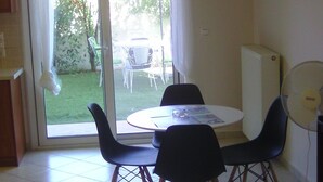 A room with a dining table and chairs, a sliding glass door leading to a patio, and a standing fan. - Remarkable 1-bed Apartment in (Chalcis)
