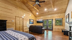 A log cabin bedroom with a bed, a sofa, a ceiling fan, and large windows. - RIVERFRONT! EASY DRIVE TO GATLINBURG AND PIGEON FORGE! GAMEROOM! MOVIE THEATER! (Sevierville)