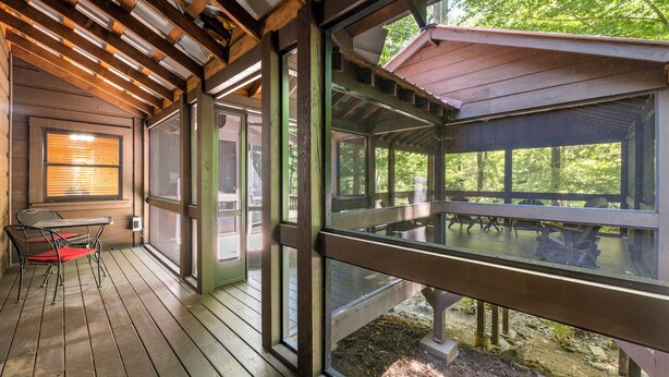 A covered outdoor deck with wooden flooring, large windows, and a table with chairs. - RIVERFRONT! EASY DRIVE TO GATLINBURG AND PIGEON FORGE! GAMEROOM! MOVIE THEATER! (Sevierville)