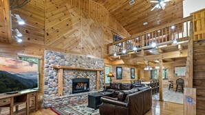 A spacious living room with a stone fireplace, leather sofa, and a dining area with wooden furniture. - RIVERFRONT! EASY DRIVE TO GATLINBURG AND PIGEON FORGE! GAMEROOM! MOVIE THEATER! (Sevierville)