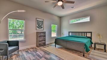 A bedroom with a bed, a desk, a chair, a ceiling fan, and two windows.