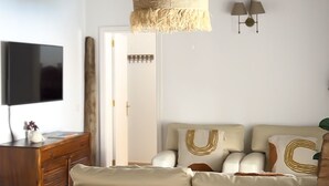 Ein Wohnzimmer mit einer Couch, einem Fernseher, einem Holzkasten und einer Pendelleuchte.