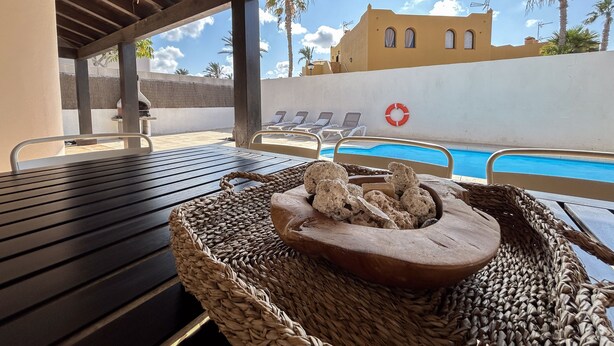 Ein Poolbereich mit Holztisch, einem Korbwägelchen voller Snacks und Liegestühlen.